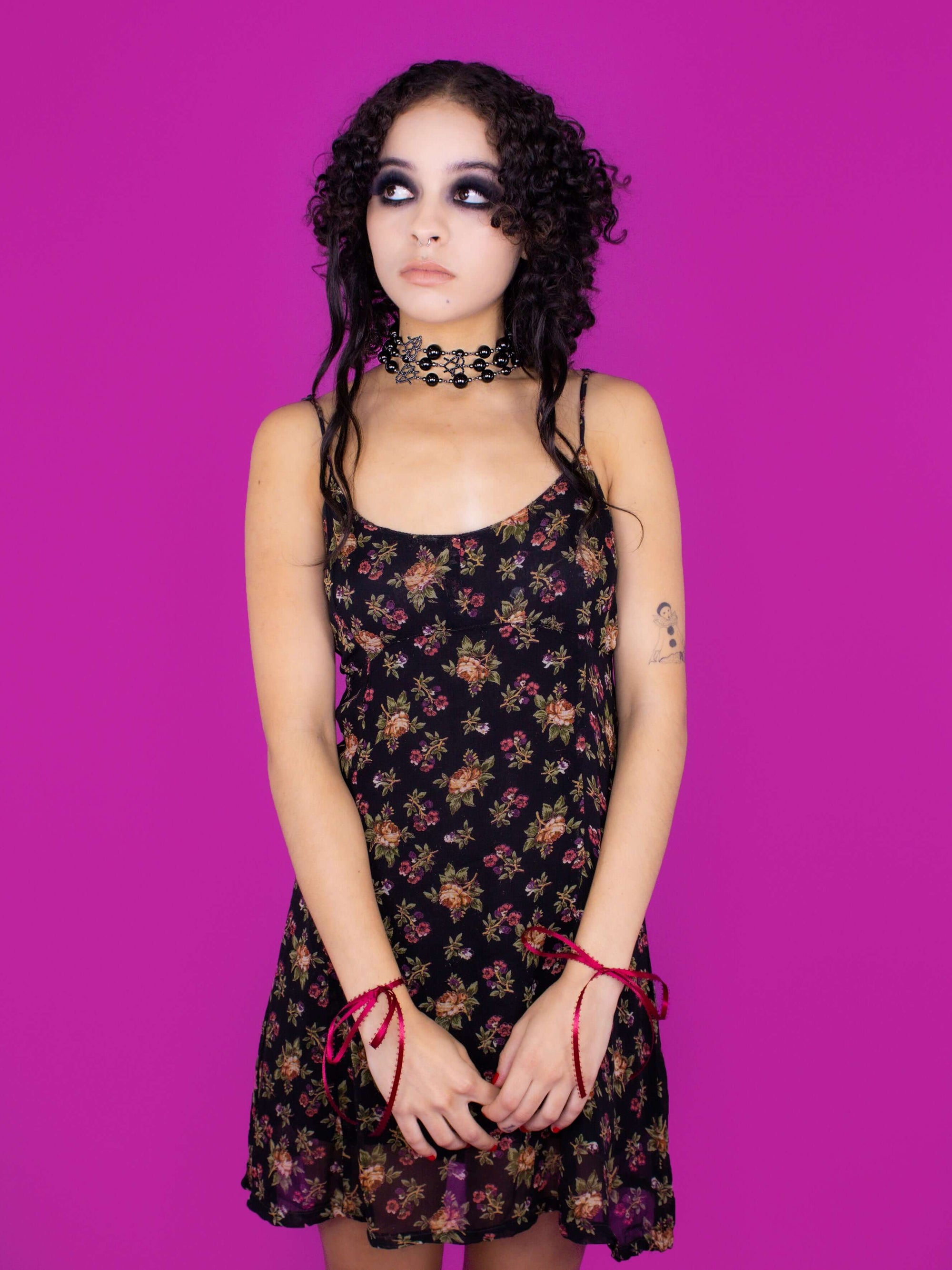 Further shot of model with necklace wrapped three times, styled in black floral dress with ribbons tied at wrists